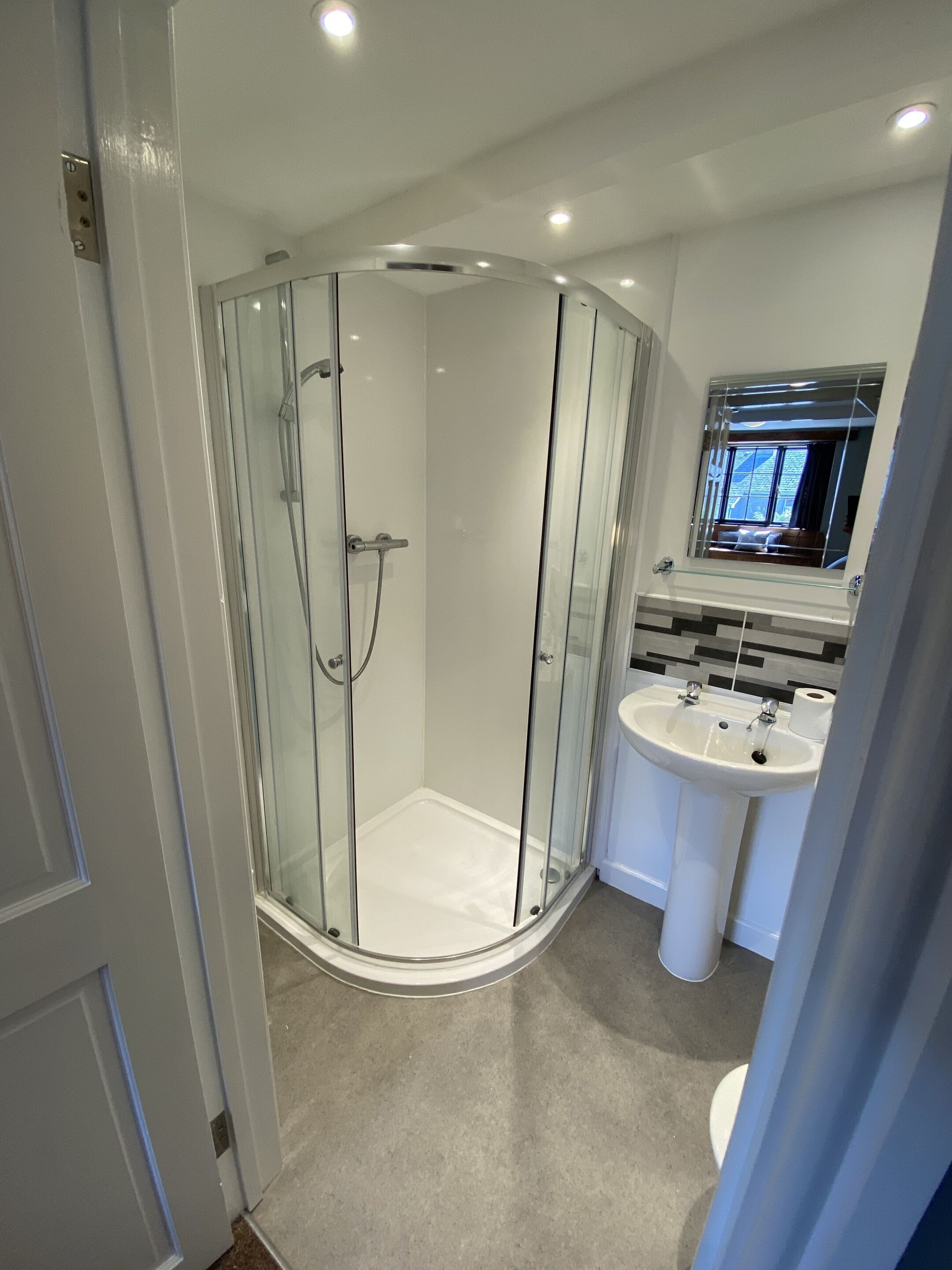 A modern bathroom with a glass-enclosed shower, a white sink, and a mirror above the sink.