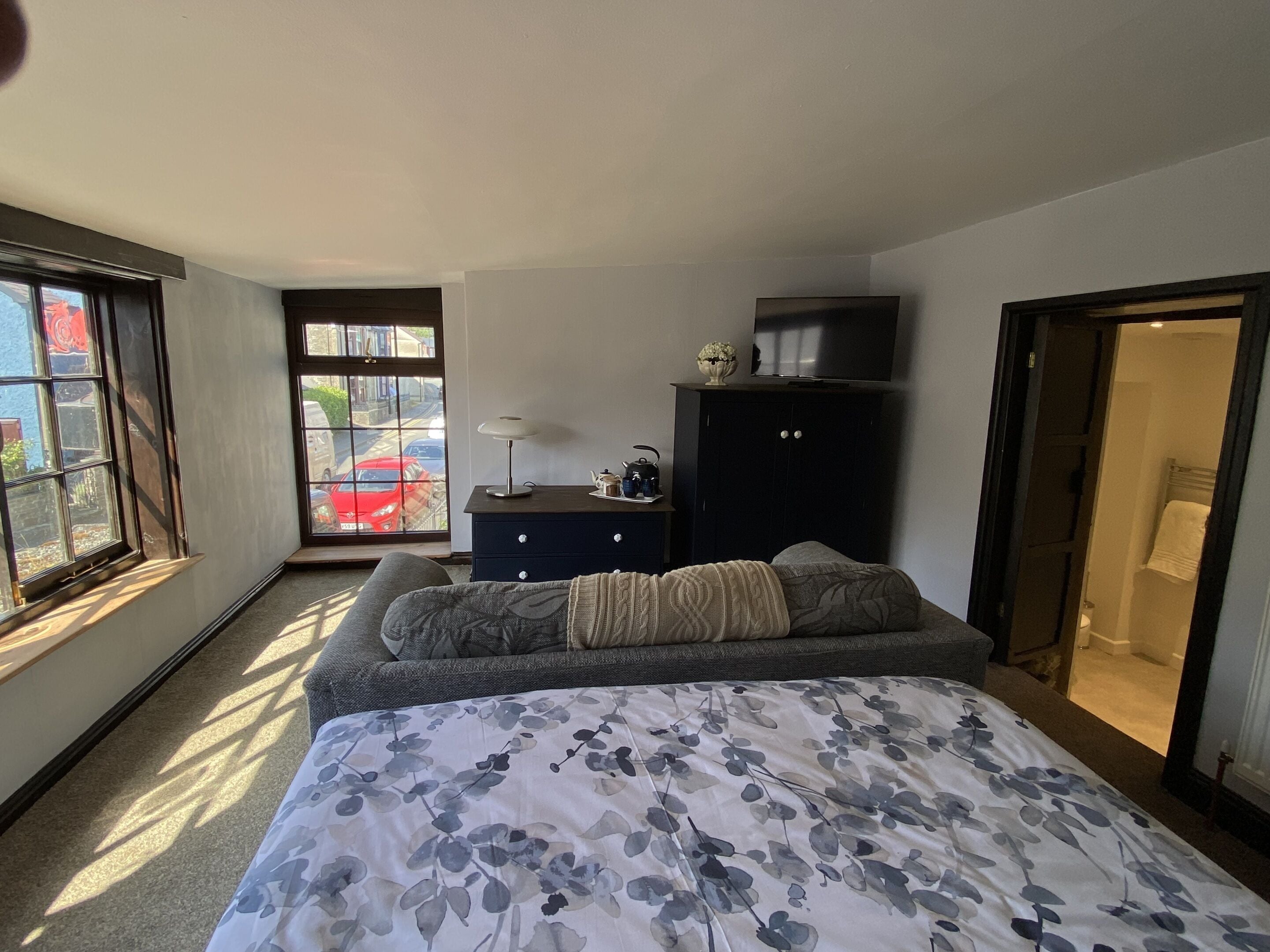 A bedroom with a bed, a dresser, a TV, and a window with a view of the street.