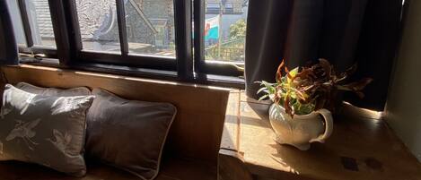 A wooden bench with cushions, a potted plant, and a window with curtains.