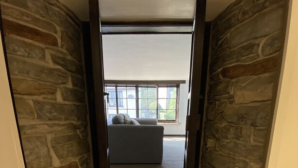 A hallway with stone walls and a carpeted floor leading to a room with a bed and a window. - Tom's of Tregaron (Tregaron)