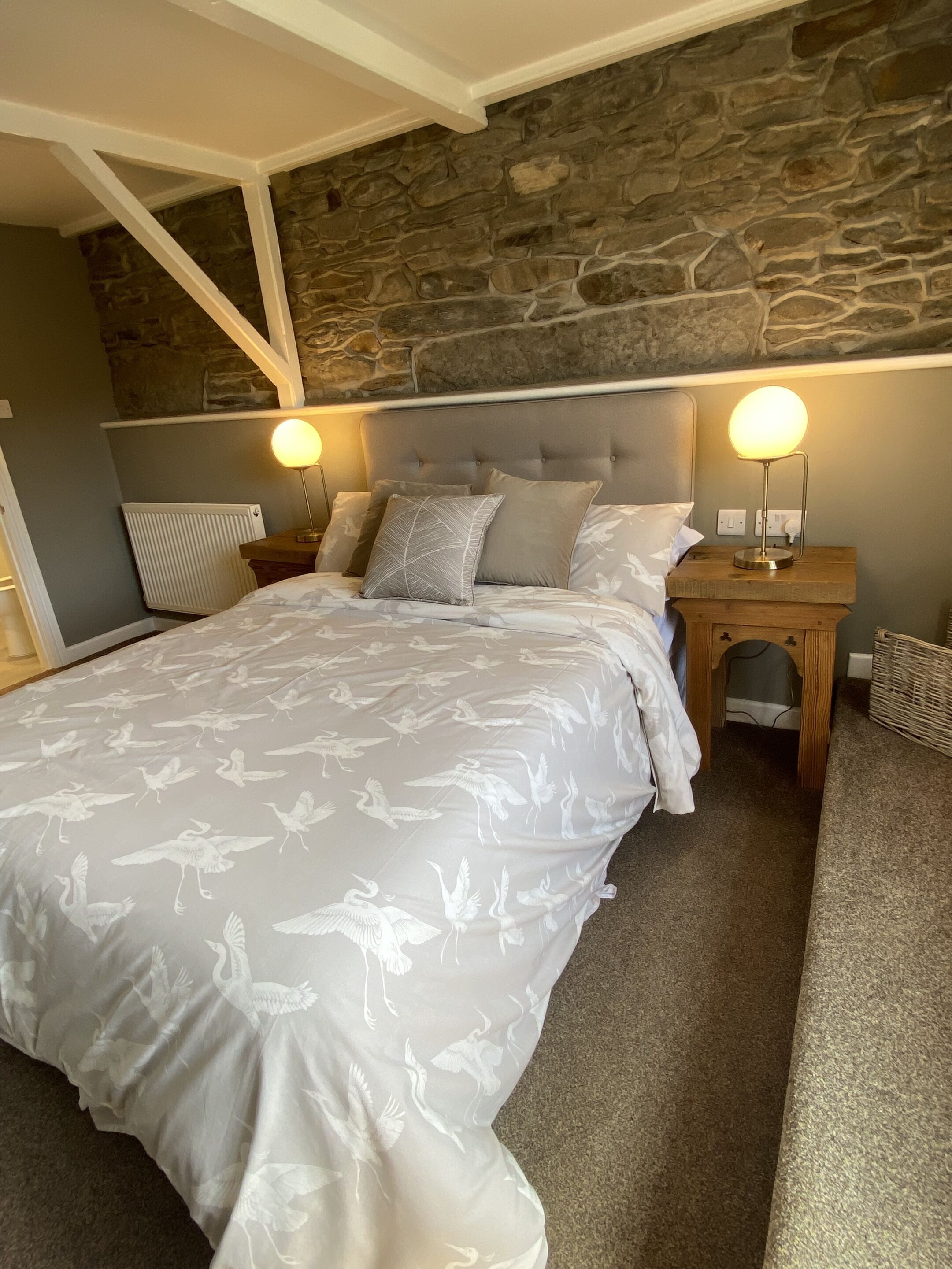 A bedroom with a large bed, stone wall, two bedside tables with lamps, and a wooden headboard.