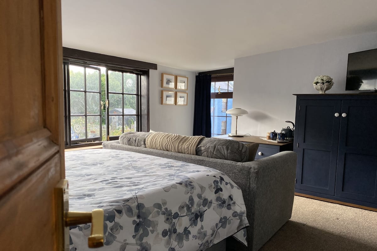 Une chambre à coucher comprenant un lit, un bureau, une armoire et une fenêtre donnant sur un paysage verdoyant.