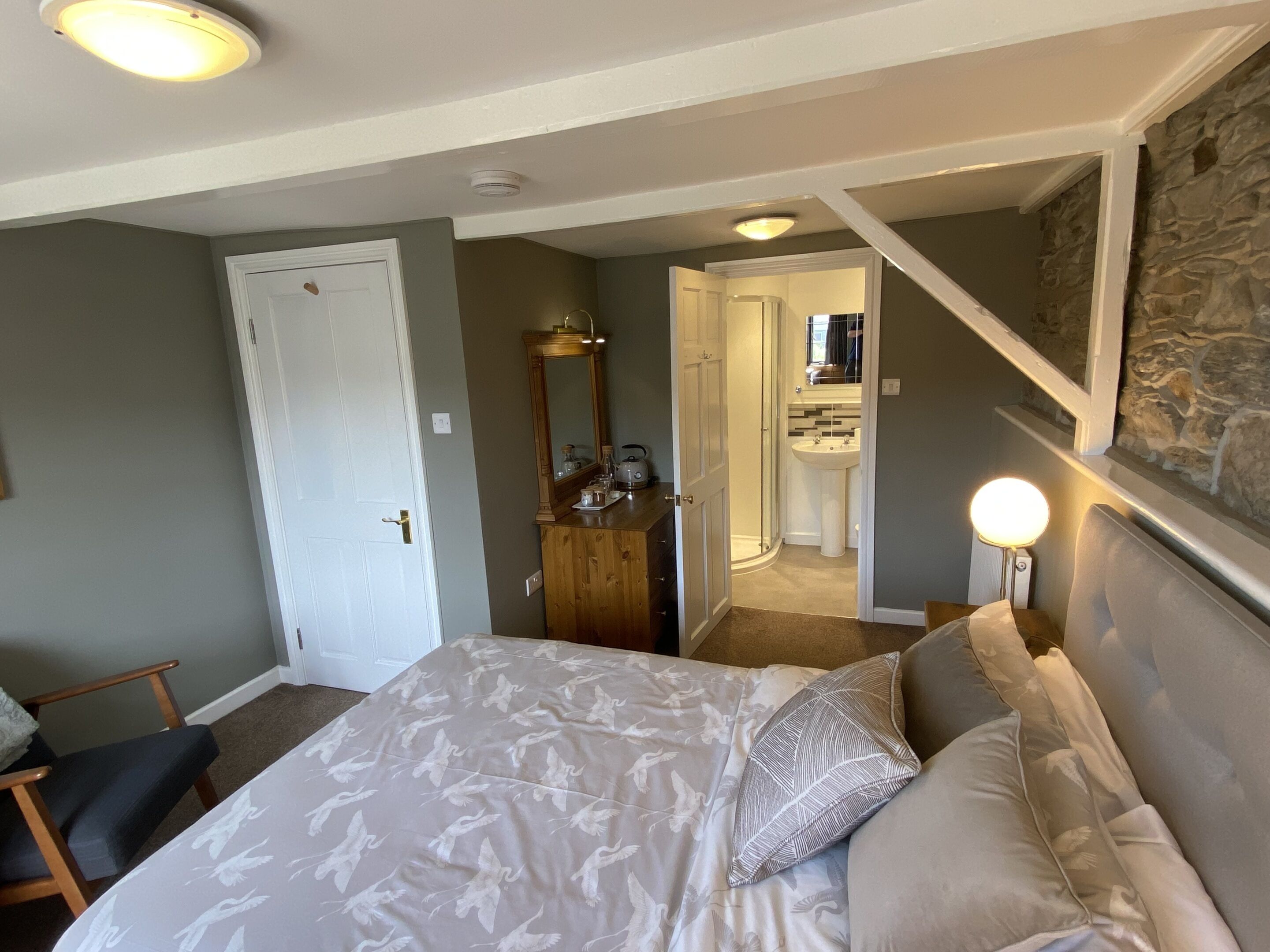 A bedroom with a bed, a dresser, a mirror, a nightstand, and a bathroom visible through an open door.