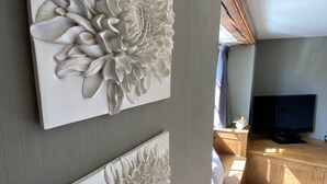 A room with two large white floral wall art pieces, a wooden TV stand, and a window with sunlight. - Tom's of Tregaron (Tregaron)