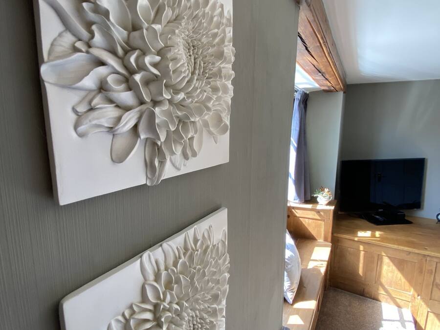 A room with two large white floral wall art pieces, a wooden TV stand, and a window with sunlight.