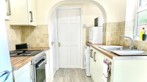 Cocina estrecha con encimera de madera, estufa, lavabo y una puerta blanca.