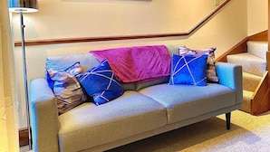 Una sala de estar con un sofá, una lámpara de pie y una escalera.