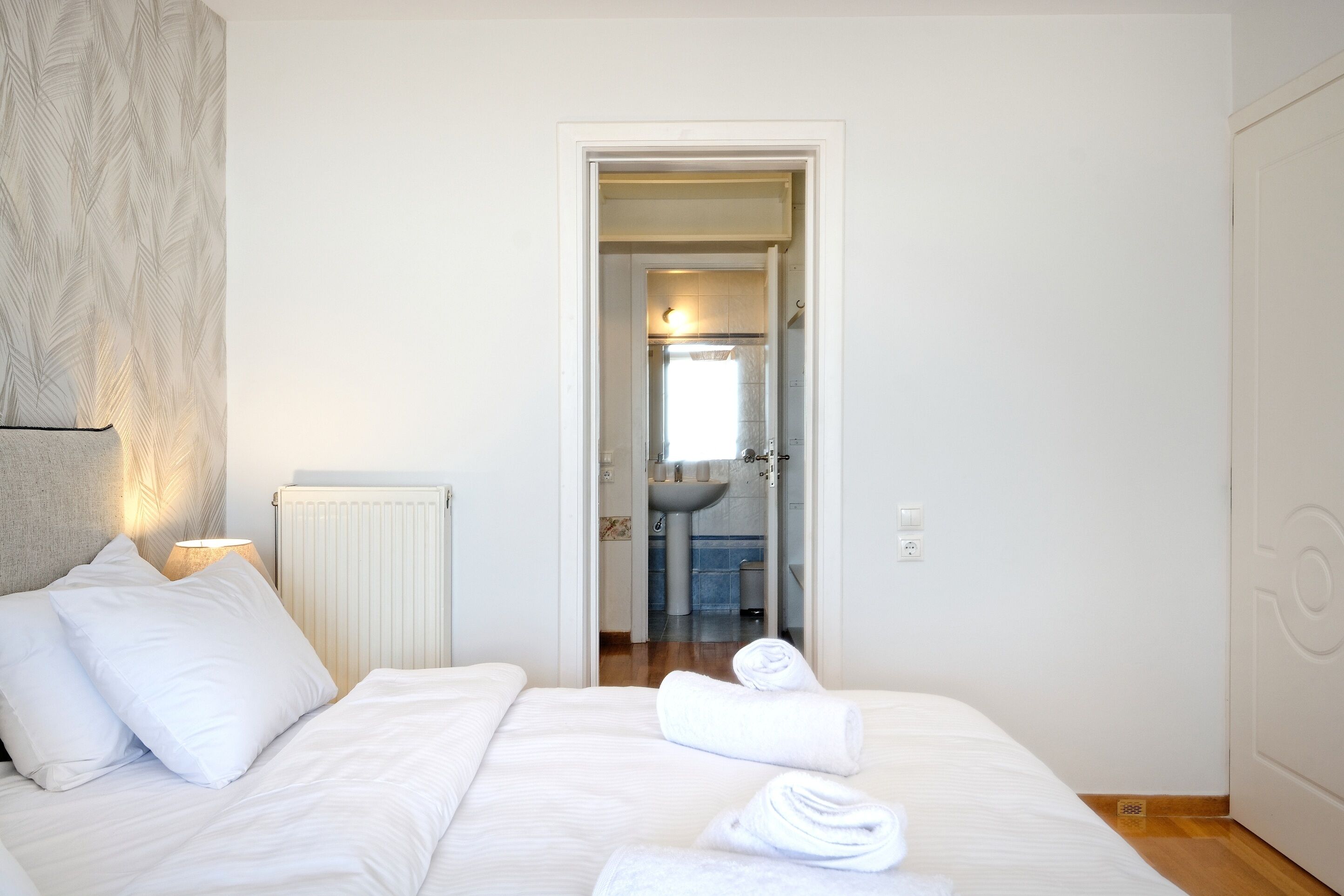 Une chambre d’hôtel avec un lit, des oreillers, une lampe, un radiateur et une vue sur la salle de bain.