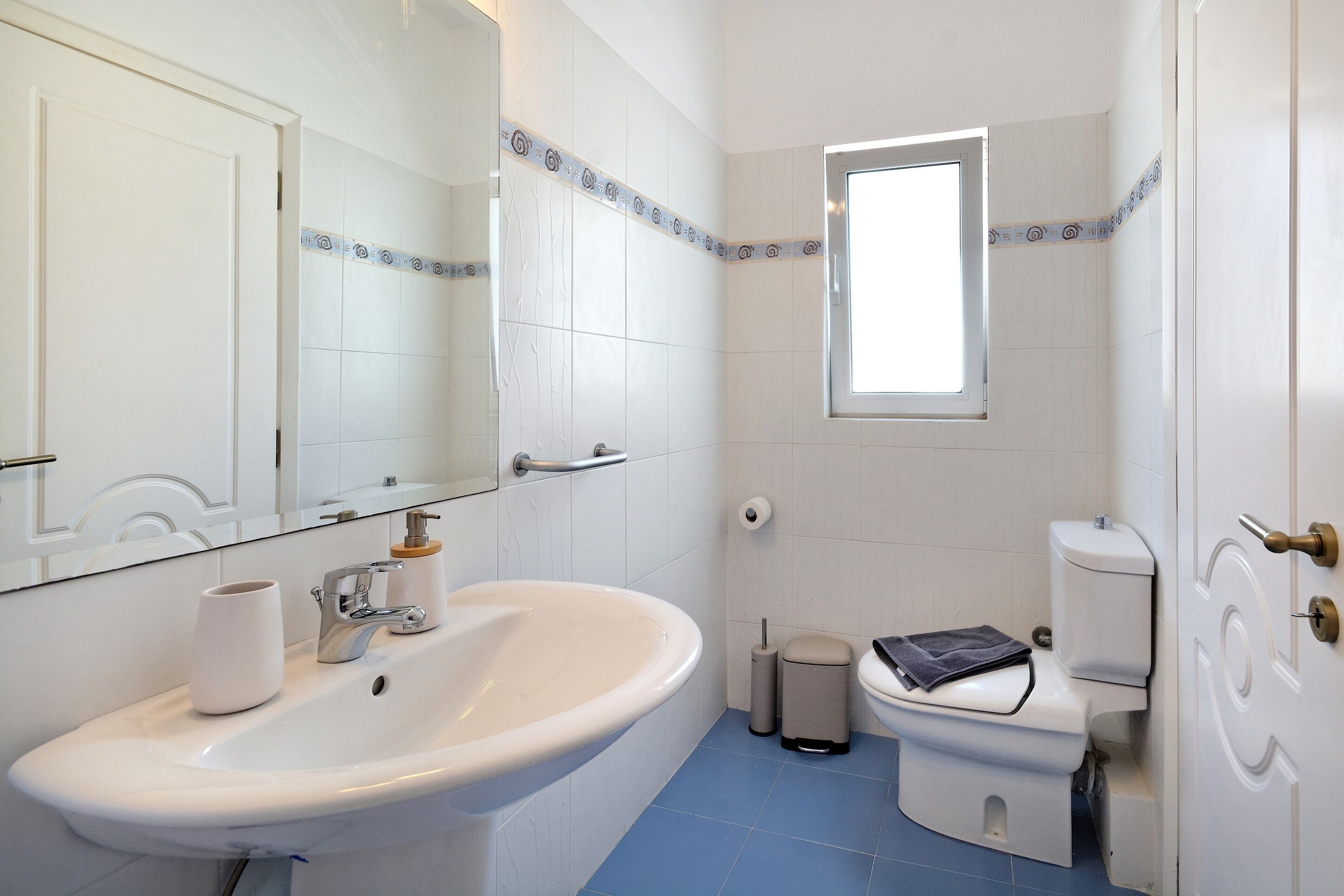 Een badkamer met een witte wasbak, een spiegel, een toilet en een raam.