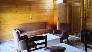 Ein gemütlicher Raum mit Holzwänden, einem Sofa, zwei Stühlen, einem Tisch und einer Tür.