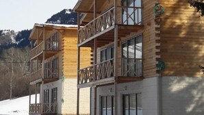Eine Holzhütte mit mehreren Balkonen und großen Fenstern vor einer verschneiten Landschaft mit Bergen im Hintergrund.