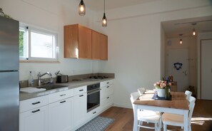 A modern kitchen with white cabinets, a stainless steel refrigerator, a built-in oven, and a dining area with a wooden table and white chairs.