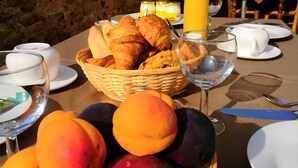 Una mesa de desayuno con cruasanes, una cesta de fruta y una botella de jugo de naranja.