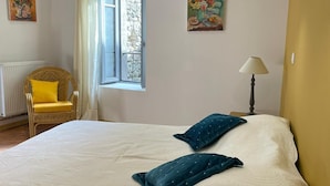 Un dormitorio con una cama grande, una ventana con cortinas, una silla y dos lámparas de pared.