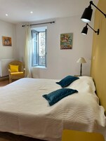 Un dormitorio con una cama grande, una ventana con cortinas, una silla y dos lámparas de pared.