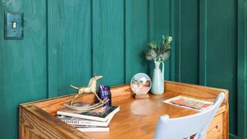 Une table en bois, sur laquelle on trouve des livres, un globe terrestre et un vase avec des plantes, le tout placé devant un mur de couleur turquoise.