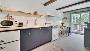 Una cocina moderna con armarios oscuros, una encimera blanca y un horno empotrado. Hay una zona de comedor con mesa y sillas, y un amplio ventanal con vistas al exterior.