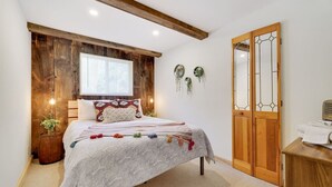 Un dormitorio con techo de madera, una cama con manta blanca, un armario de madera y una ventana con persianas.