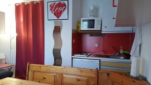 Une cuisine compacte équipée d’un four à micro-ondes, d’une machine à café et d’un évier. Un rideau rouge et un panneau décoratif avec le mot « Love » sont visibles.