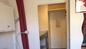 Une petite pièce avec un lit superposé, un rideau rouge, une armoire blanche et un tapis rouge.