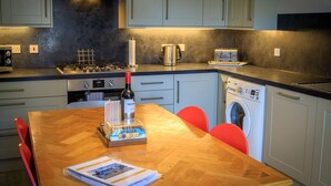 Une cuisine moderne avec une table à manger en bois, des chaises rouges, une cuisinière à gaz, une machine à café, un lave-linge et une bouteille de vin.