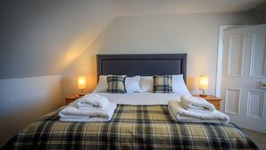 Un lit bien fait, recouvert d’une couverture à carreaux, avec deux lampes de chevet et des serviettes pliées posées sur le lit.