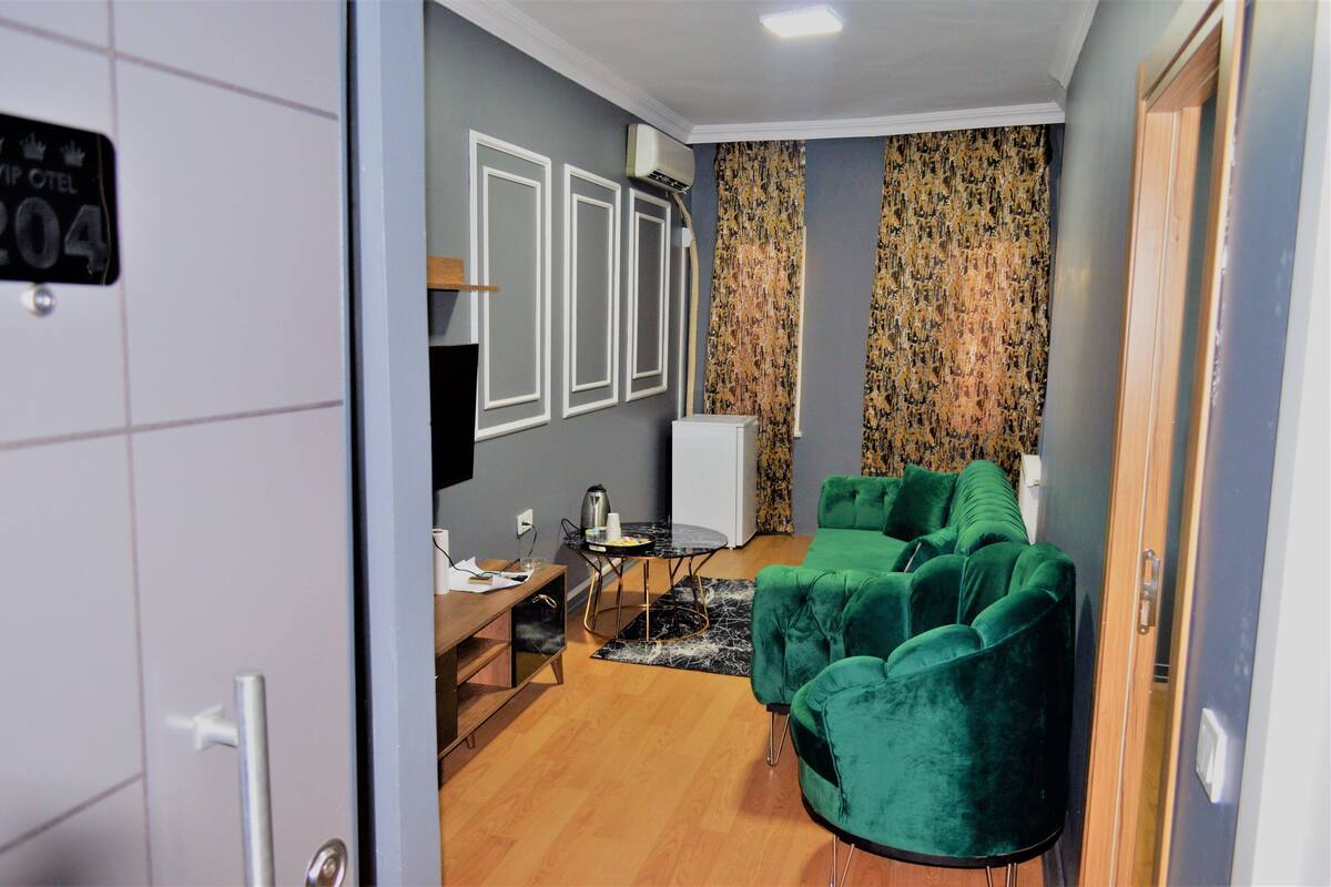 Un espace de vie compact comprenant un canapé vert, une petite table avec une bouilloire et un téléviseur.