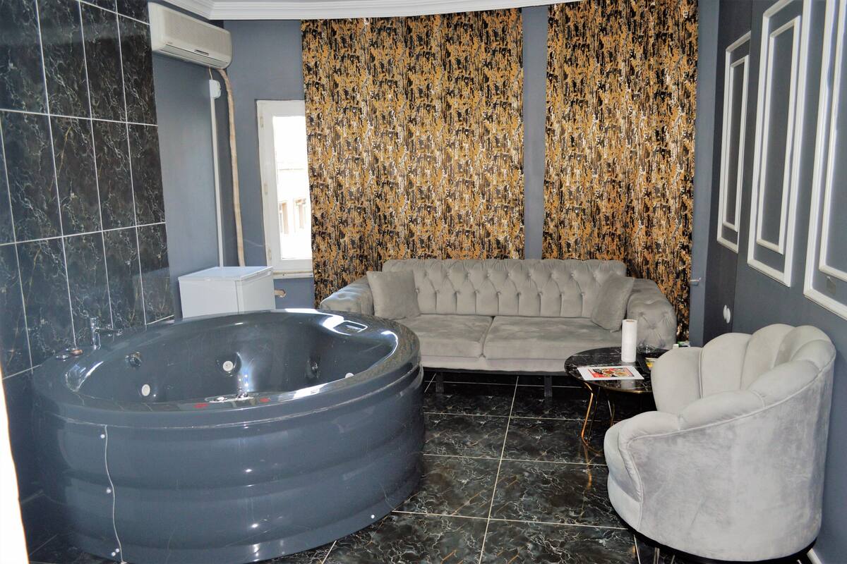 Une salle de bain avec une grande baignoire, un canapé gris et un fauteuil blanc.