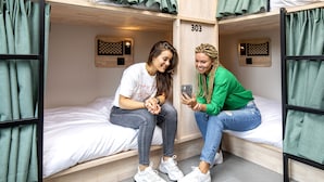 Une chambre de dortoir avec des lits superposés, le numéro « 303 » peint sur le mur et une petite étagère sur laquelle se trouvent un téléphone et un objet décoratif.