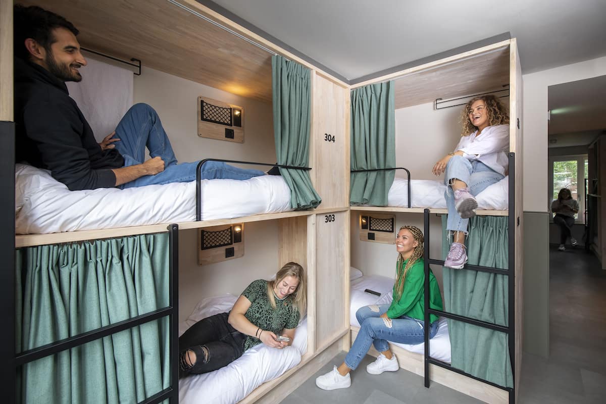 Una habitació tipo dormitori amb llits superposats, cadascun amb cortina i una petita prestatgeria.