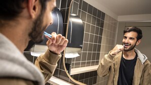 Une personne se brosse les dents dans une salle de bain équipée d'un miroir, d'un porte-serviettes et d'un mur carrelé.