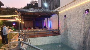 An outdoor stage with seating and a performance area, surrounded by a wall with a mosaic pattern. - Twin Towers  (Greater Noida)