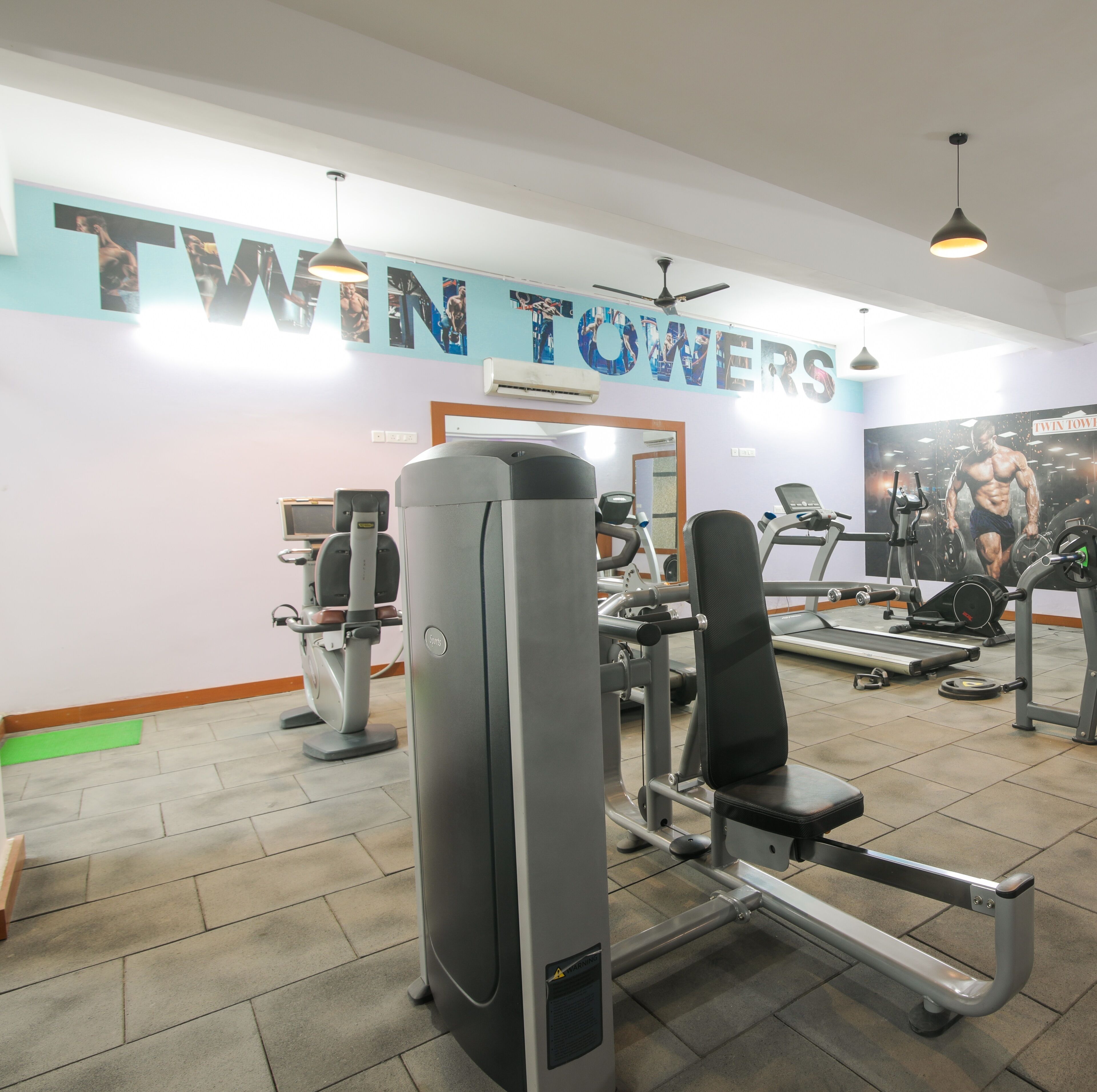 A gym with various exercise equipment, a wall with 'TWIN TOWERS' text, and a treadmill.