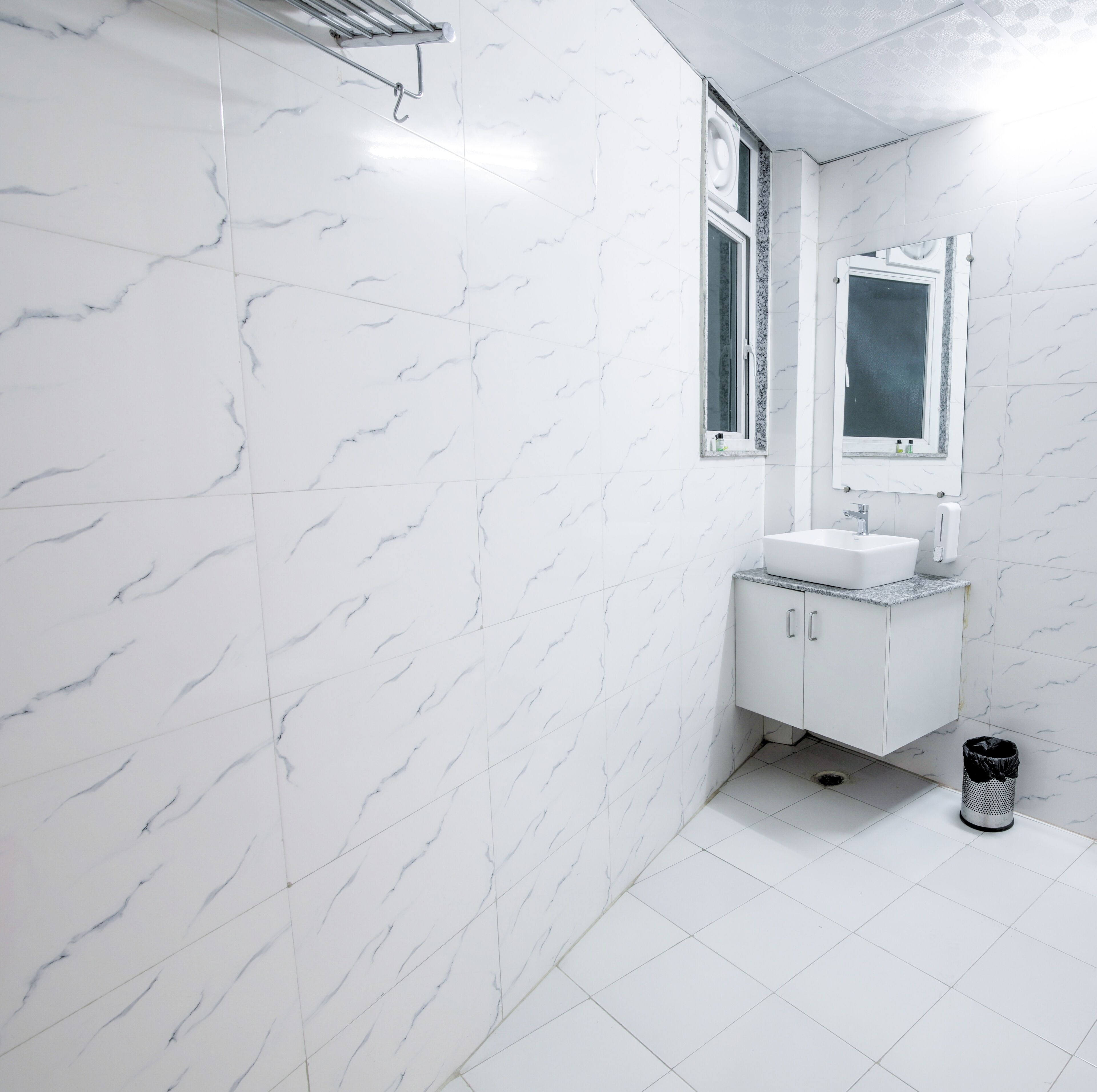 A bathroom with white marble walls and floor, a white sink, and a mirror above it.