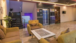 A lobby with a reception desk, a staircase, and a seating area with sofas and a coffee table. - Twin Towers  (Greater Noida)