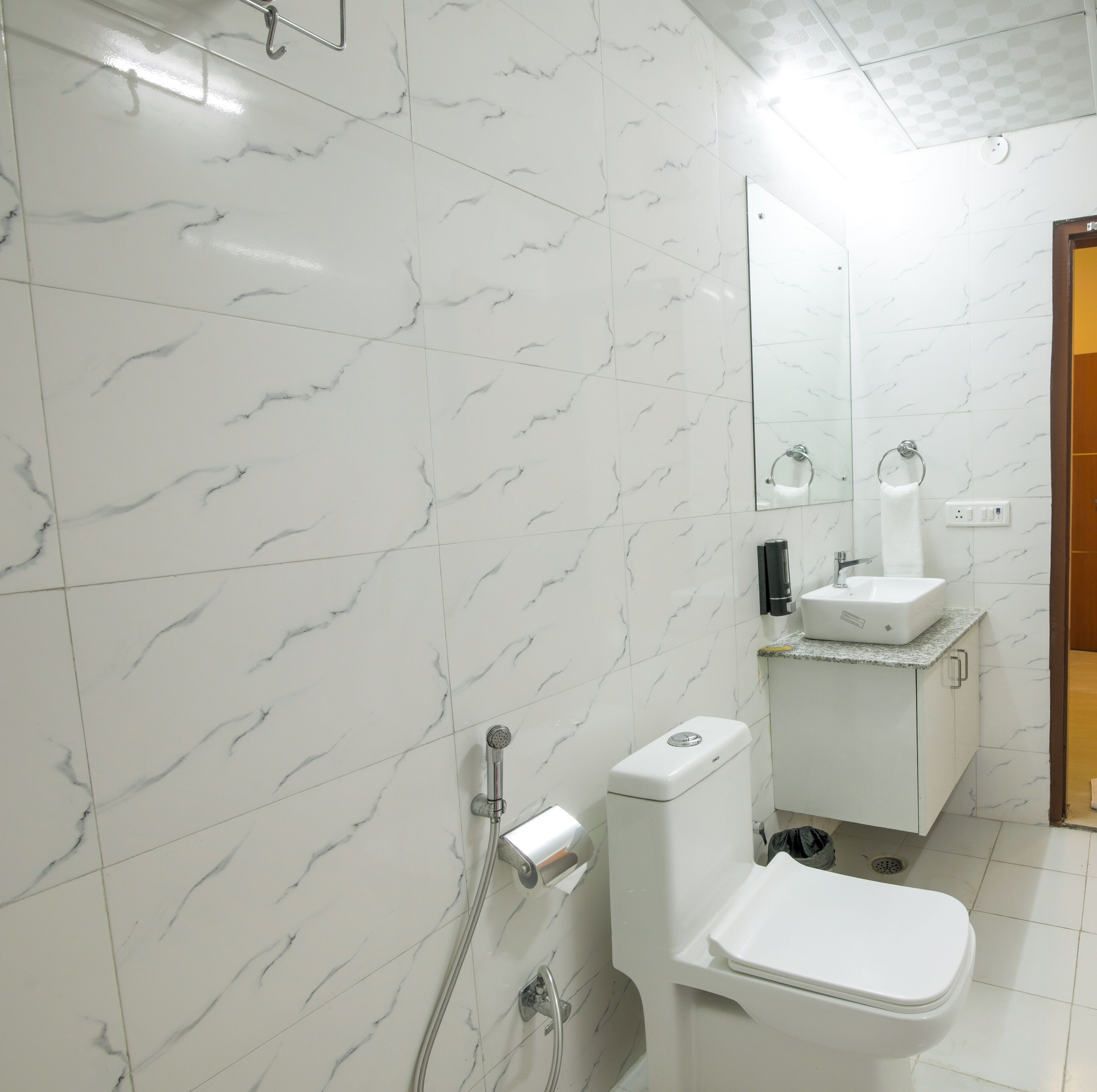 Un baño con baldosas de mármol blanco, inodoro blanco, lavabo con encimera y un espejo sobre él.