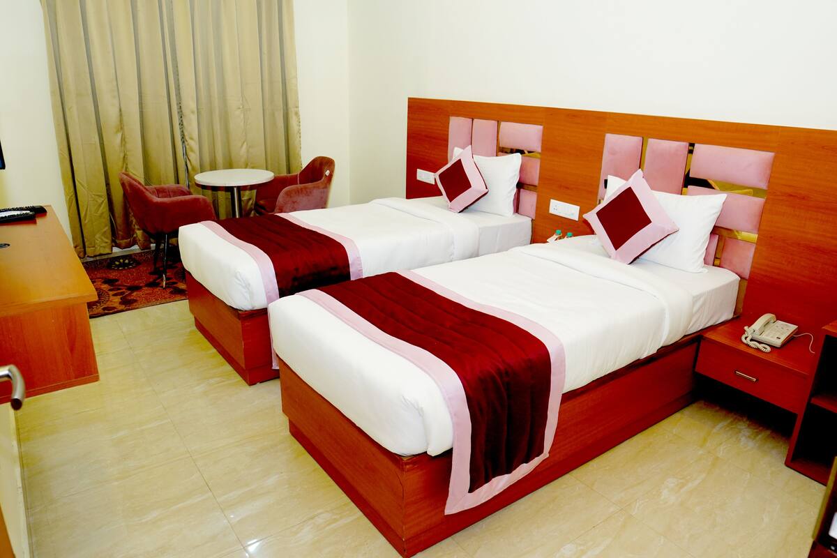 Habitación de hotel con dos camas, una mesita redonda, un sillón rojo y una mesita de noche con un teléfono.