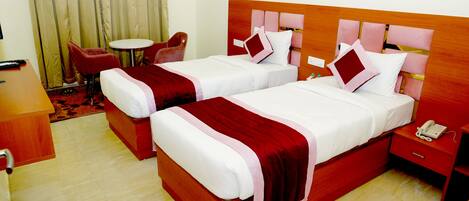 A hotel room with two beds, a small round table, a red armchair, and a bedside table with a phone.
