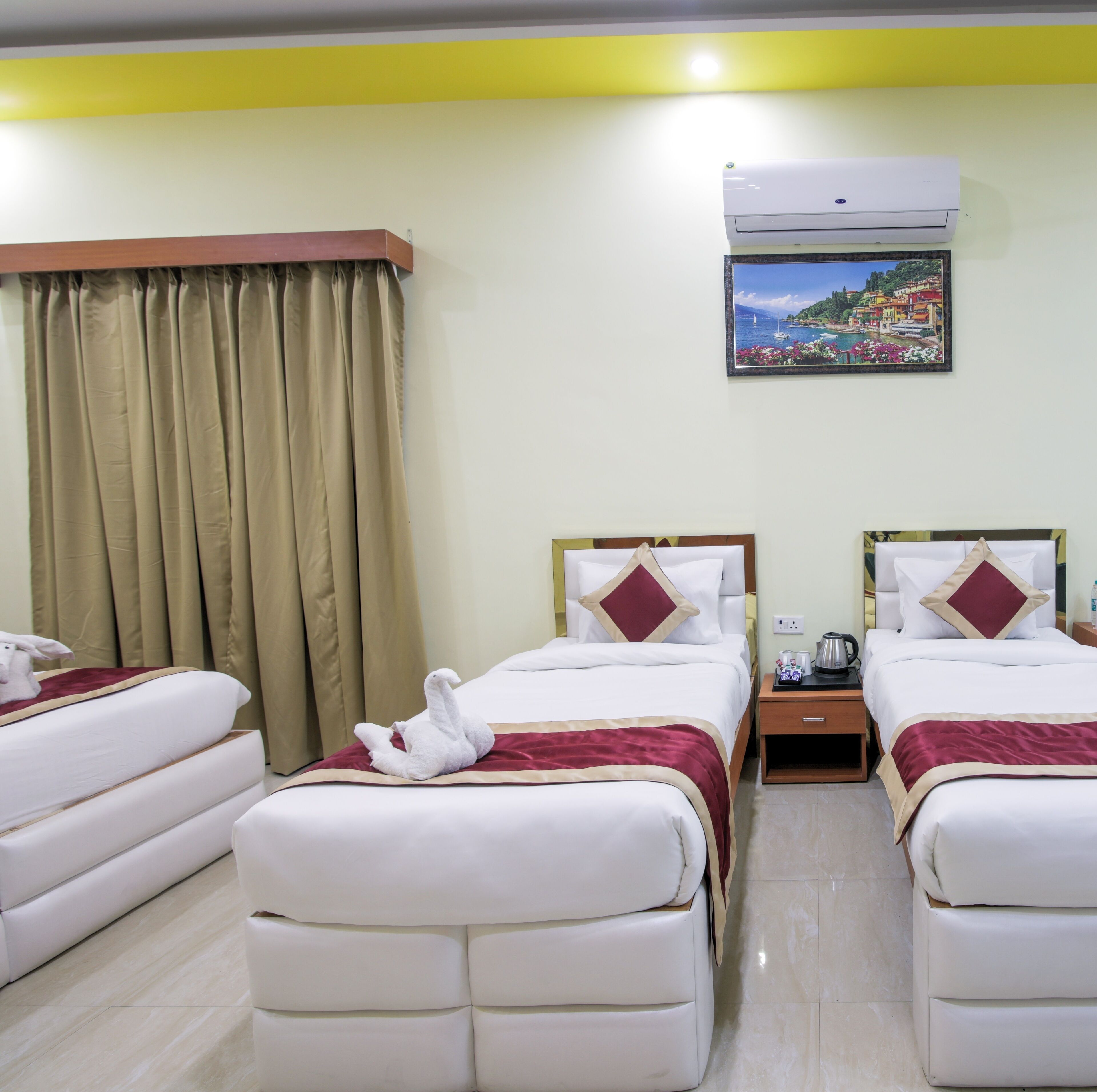 Habitación de hotel con dos camas, cortinas color beige, un cuadro de un pueblo costero y un equipo de aire acondicionado.