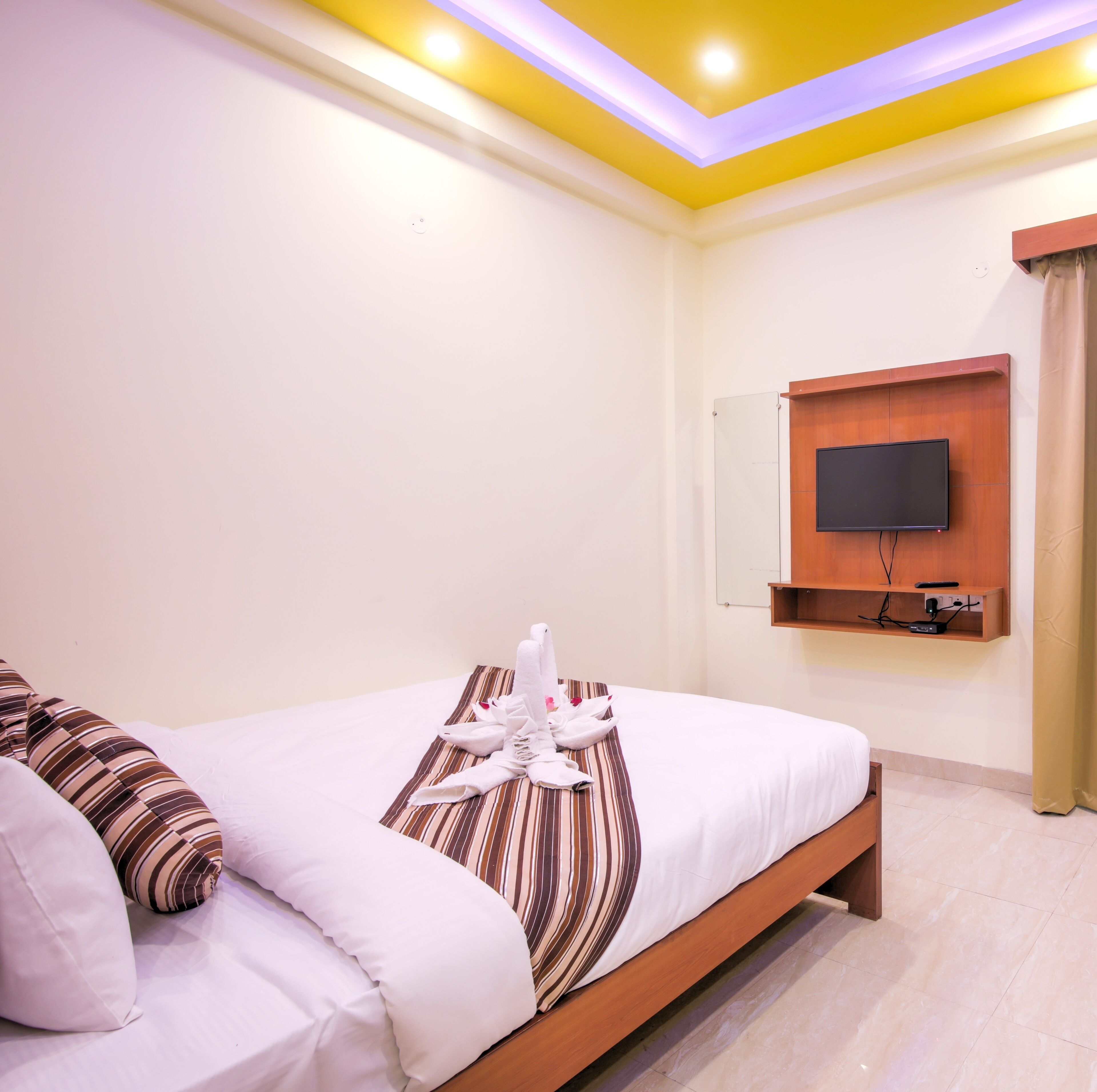 A hotel room with a bed, pillows, a TV, and a wooden shelf.