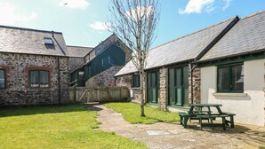 A stone building with a green door and windows, a grassy yard, a stone pathway, and a picnic table. - Ramsey Cottage (Haverfordwest)