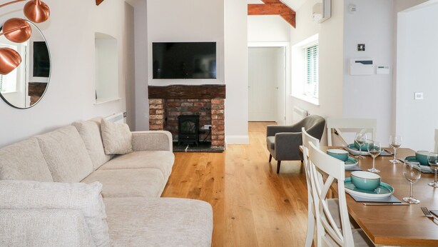 A spacious living area with a sofa, a dining table set with teal plates, and a fireplace. - Ramsey Cottage (Haverfordwest)