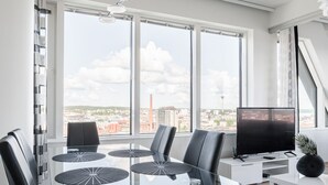 Un salón moderno con una mesa de comedor de vidrio, sillas negras, un televisor de pantalla plana y grandes ventanales con vistas a la ciudad.