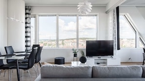 Una sala de estar moderna con un ventanal grande, un televisor de pantalla plana, un comedor con mesa de vidrio y un sofá gris.
