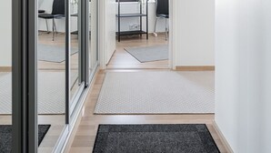 Un interior moderno con una puerta de vidrio que da a un espacio con un escritorio y una silla, una pared blanca con un aviso y suelo de madera.