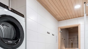 Lavandería con lavadora y secadora de carga frontal, un calentador pequeño y una sauna de madera.