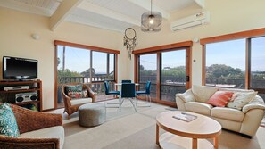 Amplia sala de estar con televisor, zona de estar y ventanas grandes con vistas al exterior.