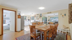 Un grand espace à manger avec une table et des chaises en bois, une cuisine à l’arrière-plan et une vue sur un balcon.