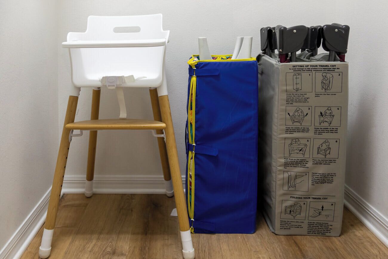 Uma cadeira branca com bandeja, um bercinho de viagem azul com manual e um conjunto de facas.