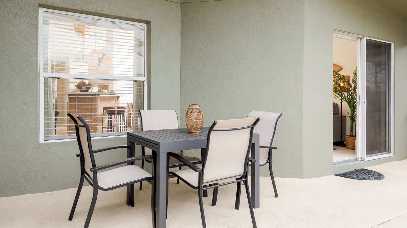 A patio with a table and chairs, a window, and a door leading to an interior space.